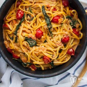 Photo of linguine in a pan with spinach, cherry tomatoes and pink vegan sauce. A recipe from All About Vegans.