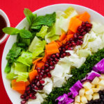 Photo of a colorful festive fresh salad for holiday dinners with pomegranate, white and purple cabbage, lettuce, dill, raisins, apple, carrot and mint