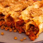 A photo of cooked cannelloni stuffed with lentils, vegetables and tomatoes with almond milk and tomatoe sauce. A vegan recipe from All About Vegans.