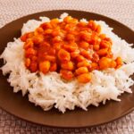 Photo of a plate with rice and chickpeas with red sauce on top. A vegan recipe of rice and chickpeas in curry and almond milk sauce called Chana Masala or Chole Masala).