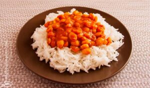 Photo of a plate with rice and chickpeas with red sauce on top. A vegan recipe of rice and chickpeas in curry and almond milk sauce called Chana Masala or Chole Masala).