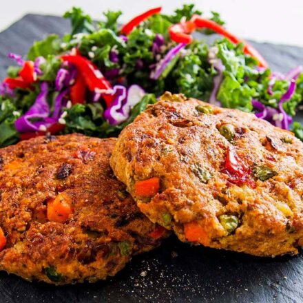 Photo of two patties served with kale salad and a lemon slice. Grilled potato vegetables patties. A vegan and vegetarian recipe from All About Vegans.