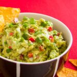 A photo of a Mexican guacamole dip served with nachos. A vegan recipe from All About vegans.