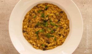A white plate from a top view, with mushrooms turmeric risotto. A vegan and vegetarian recipe from All About Vegans.
