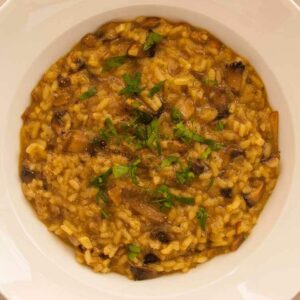 A white plate from a top view, with mushrooms turmeric risotto. A vegan and vegetarian recipe from All About Vegans.