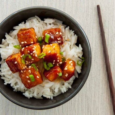 Photo of a vegan dish of general Tso's tofu with basmati rice in a bowl and a pair of chopsticks.