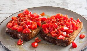 Φωτογραφία από δύο vegan μπρουσκέτες (φρυγανισμένες φέτες ψωμιού τριμμένες με σκόρδο) σερβιρισμένες με ντομάτα, σκόρδο, αλάτι, ρίγανη και ελαιόλαδο. Μία vegan συνταγή από το All About Vegans.