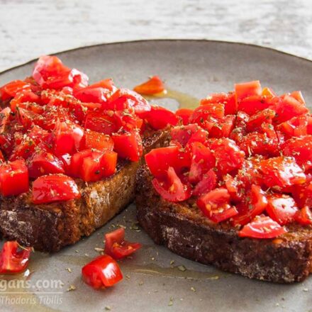 Photo of two vegan bruschetta (toasted slices of bread rubbed with garlic) served with tomato, garlic, salt, oregano and olive oil. A vegan recipe from All About Vegans.