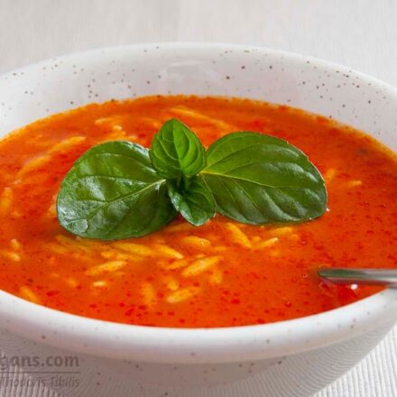 Photo bowl of tomato soup with barley and a basil leaf. A vegan and vegetarian recipe from All About Vegans.