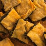 Photo with vegan pieces of Greek rustic wild greens pie and handmade filo on a cutting board. An easy, quick and enjoyable recipe from All About Vegans.