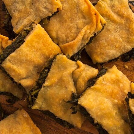 Photo with vegan pieces of Greek rustic wild greens pie and handmade filo on a cutting board. An easy, quick and enjoyable recipe from All About Vegans.