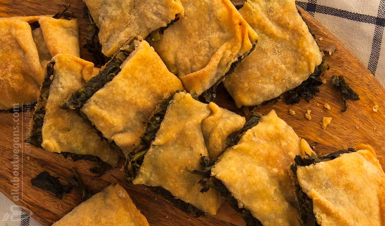 Photo with vegan pieces of Greek rustic wild greens pie and handmade filo on a cutting board. An easy, quick and enjoyable recipe from All About Vegans.