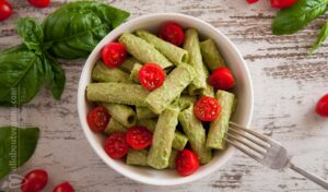 Photo of a rigatoni dish with vegan pesto and cherry tomatoes. Garnished with basil leaves and cherry tomatoes. A vegan recipe from All About Vegans.