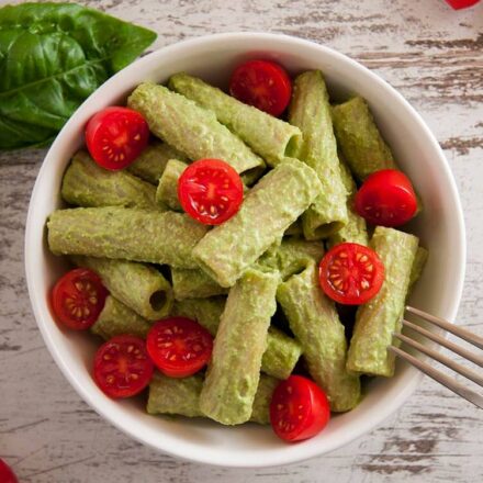 Photo of a rigatoni dish with vegan pesto and cherry tomatoes. Garnished with basil leaves and cherry tomatoes. A vegan recipe from All About Vegans.