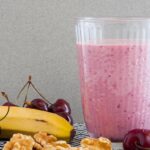 Photo of an intense vegan pink smoothie, surrounded by banana, cherries and walnuts. A vegan recipe from All About Vegans.