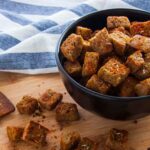 Photo of a bowl full of homemade croutons toasted in olive oil (flavored with garlic) and sprinkled with spices and herbs. A vegetarian and vegan recipe from All About Vegans.