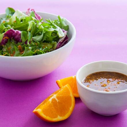 Photo of fresh green salad, with a bowl of vinaigrette sauce with orange aroma in the foreground! A vegan recipe from All About Vegans.