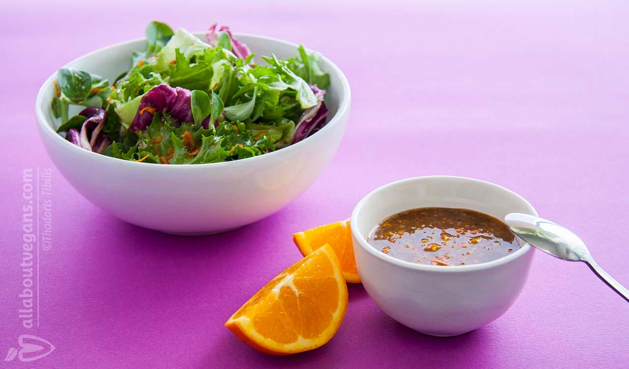 Photo of fresh green salad, with a bowl of vinaigrette sauce with orange aroma in the foreground! A vegan recipe from All About Vegans.