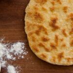 Φωτογραφία ενός τηγανόψωμου περιτρυγιρισμένου με δύο μπολ με αλεύρι και ελαιόλαδο. Μία vegan συνταγή από το All About Vegans.